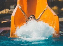 A happy woman coming off an orange waterslide making a splash as she lands in the water