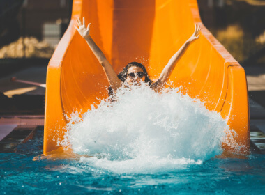 A happy woman coming off an orange waterslide making a splash as she lands in the water