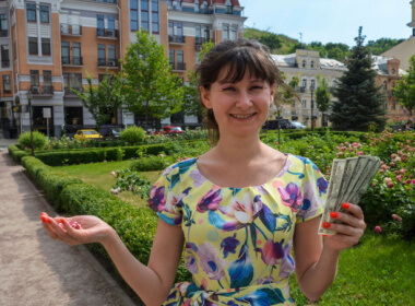 European woman smiling showing winnings from playing online casino games. In the background are old beautiful European buildings