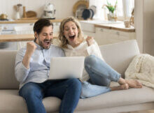 young couple gaming on their sofa at an online casino celebrating a win