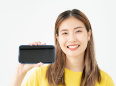 A smiling young oriental woman showing her smartphone on which she plays casino games.
