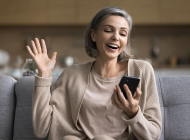 Attractive middle-aged woman enjoying something on he smartphone while comfortably siting on her sofa.