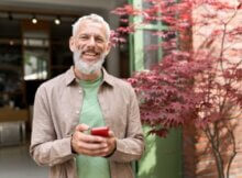 smiling older man holding a smartphone after making a smart bet at an online casino