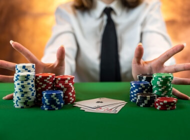 a young woman reaches for the chips after winning a poker hand with a full house. She is wearing a white shirt and a black tie.