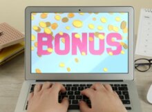 a man typing at his laptop with the word bonus in pink on the screen and gold coins floating all around