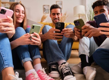 happy and smiling young adults sitting together on the floor playing on their phones