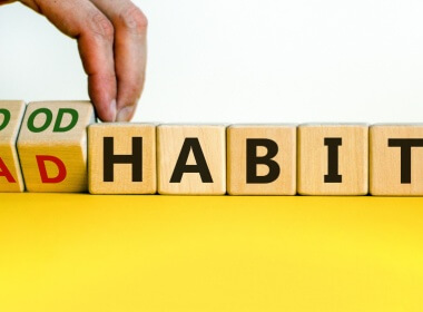 a man holding a block with word good on one side and bad on the other side and another set of blocks spelling habits